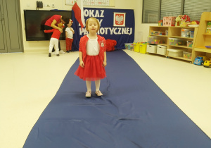 Lena ubrana na biało czerwono pozuje podczas "Pokazu mody patriotycznej" na granatowym dywanie.